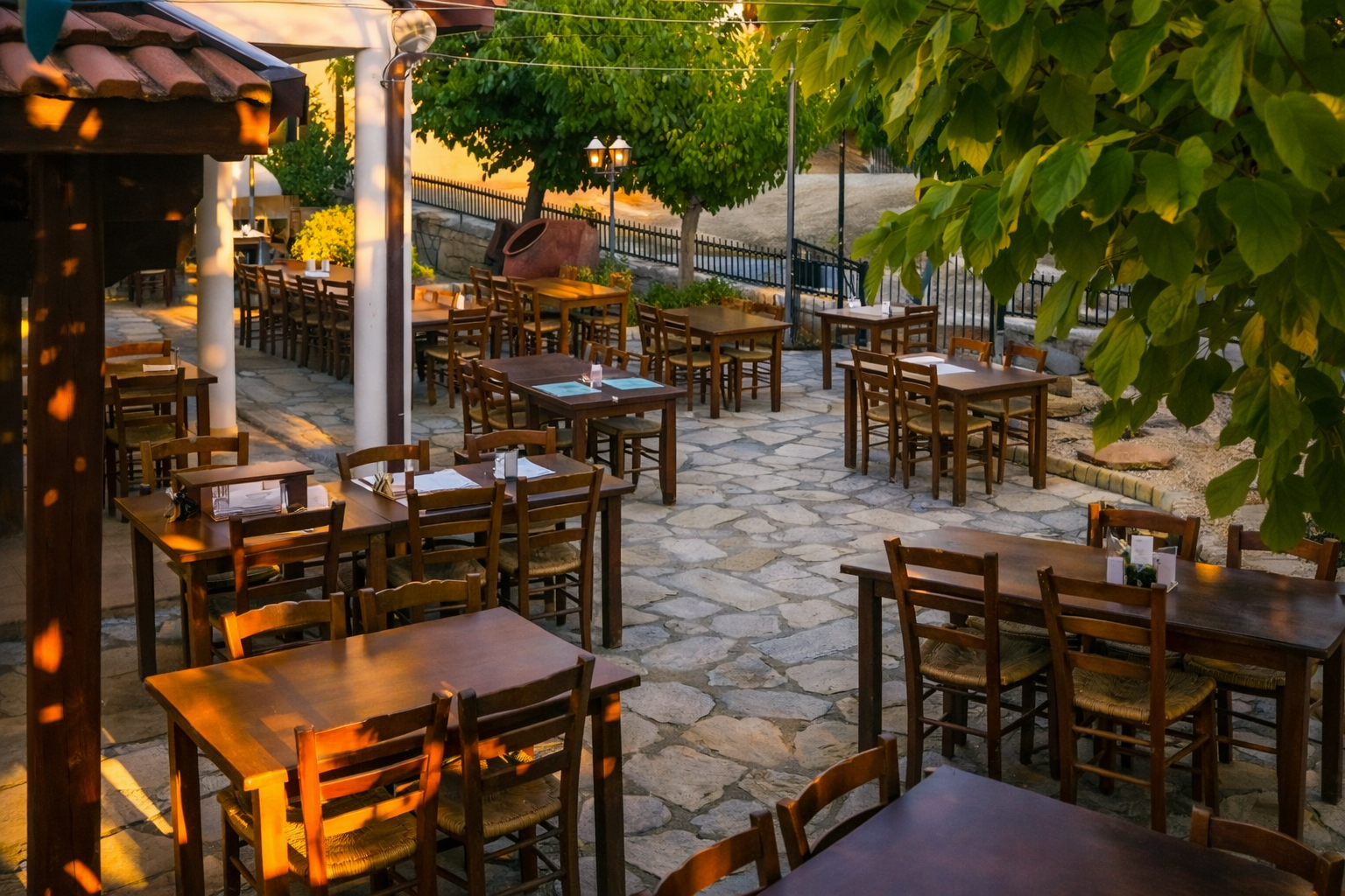 Outdoor dining area at 7 Linoi tavern in the Cypriot mountains, with wooden tables set on a stone courtyard under leafy trees